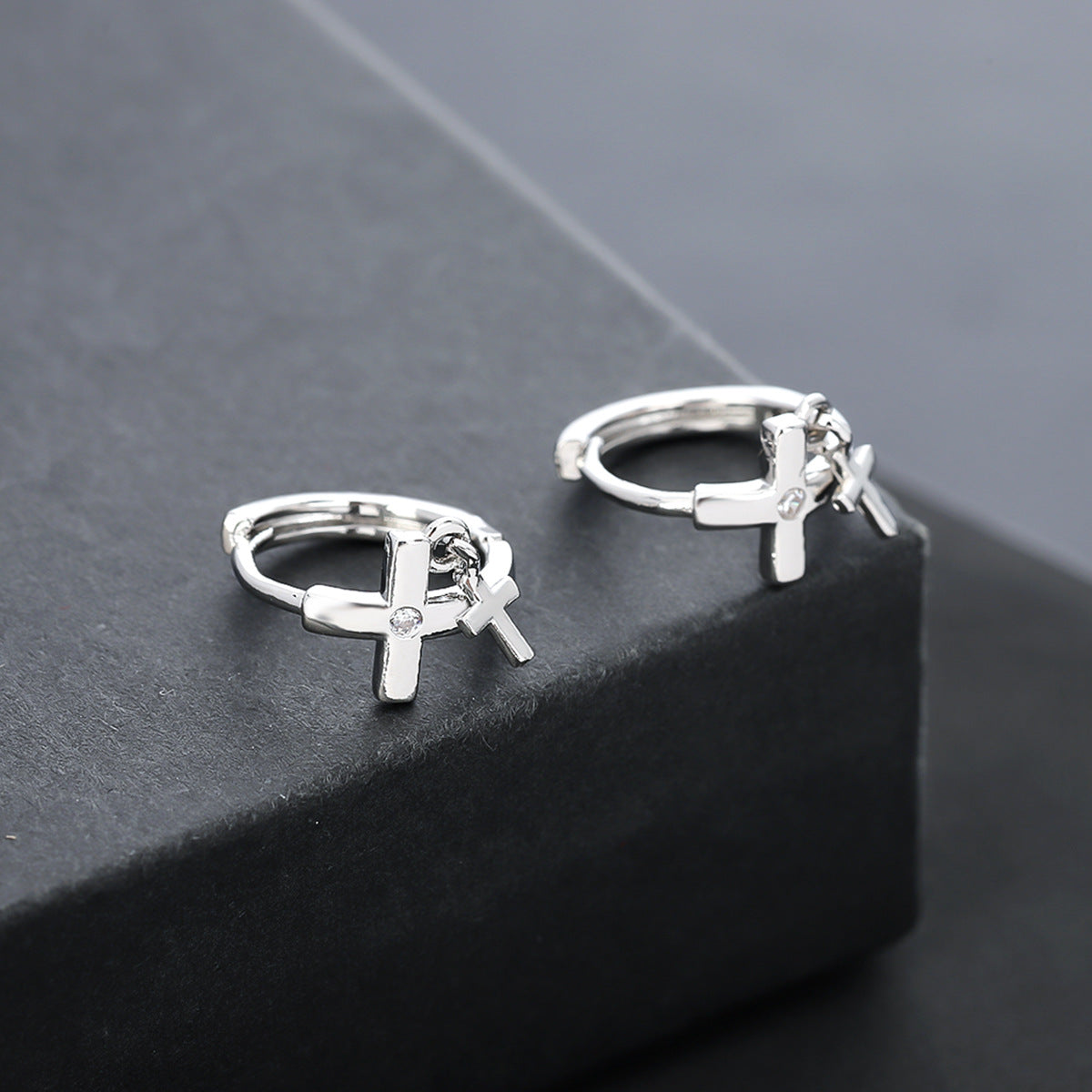 Cross charm huggie earrings on black display platform