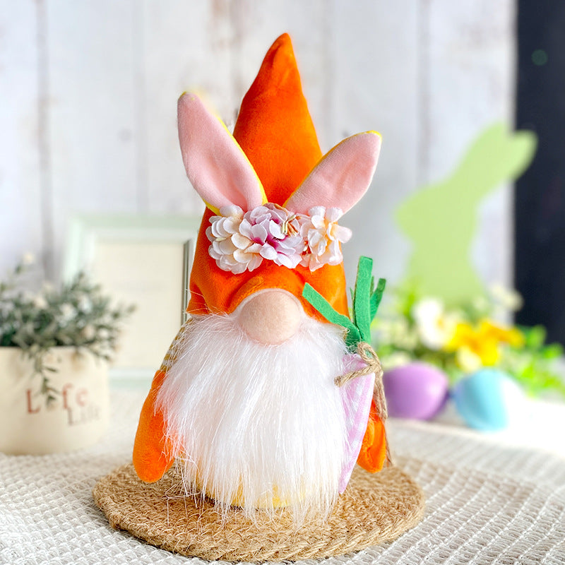 Easter gnome with a tall orange hat, pink bunny ears, floral crown, white beard, and holding a fabric carrot, placed on a woven mat.