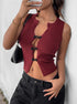 Angular view of woman in a burgundy cut-out sleeveless top and black pants, holding a phone and a black shoulder bag.