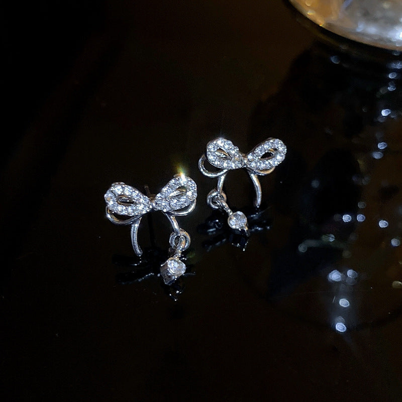 Close-up of miniature silver bow stud earrings with crystal details on dark background, showing delicate design
