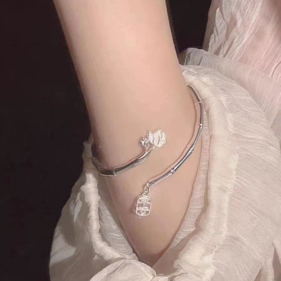 A woman wearing a silver adjustable bamboo bracelet with flower charm and pendant against white fabric backdrop
