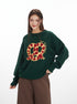 Oversized knit sweater in forest green with embroidered red and gold pretzel design and 'Year of' text