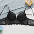 A black push-up bralette with scalloped lace trim displayed flat on white surface with denim fabric and wooden candle holder above