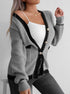 Gray knit cardigan with black trim, worn open with white tank top, woman in jeans standing against white wall