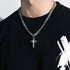 Close-up of a silver cross necklace on a thick Cuban link chain, worn over a black shirt with a white graphic design
