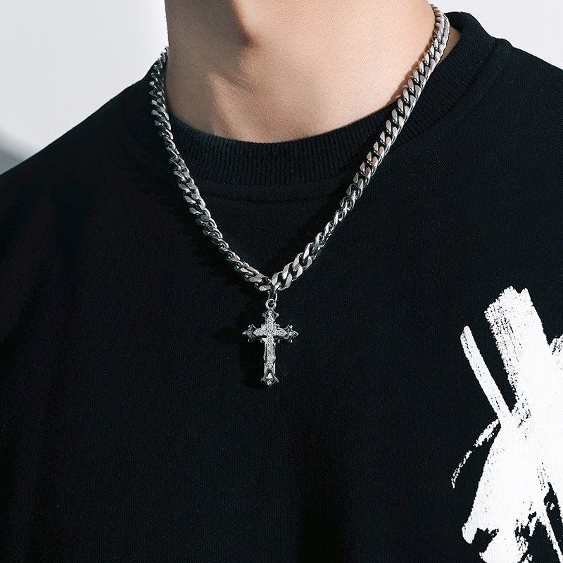 Close-up of a silver cross necklace on a thick Cuban link chain, worn over a black shirt with a white graphic design