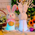 Side view and back view of two glowing Easter bunny plush toys with soft fur, one in a pink scarf holding an egg and the other in a blue bowtie holding a carrot, surrounded by Easter decorations.