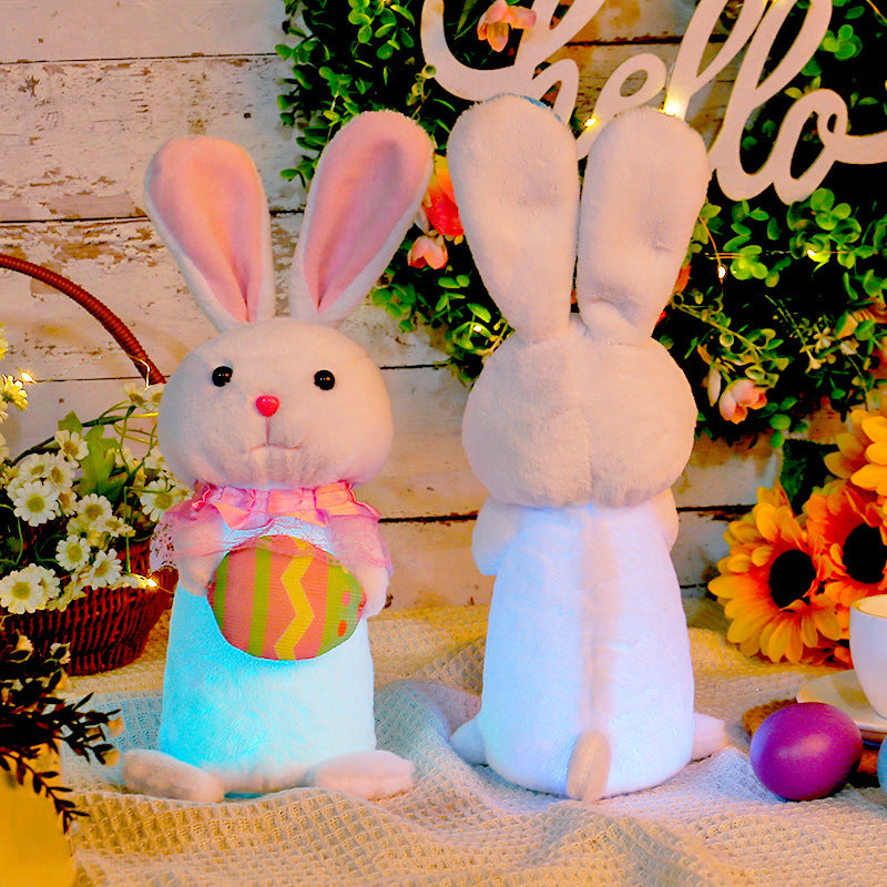 Side view and back view of two glowing Easter bunny plush toys with soft fur, one in a pink scarf holding an egg and the other in a blue bowtie holding a carrot, surrounded by Easter decorations.