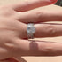A woman displaying silver engagement ring with cushion-cut diamond center and baguette diamond accents on her hand in natural light