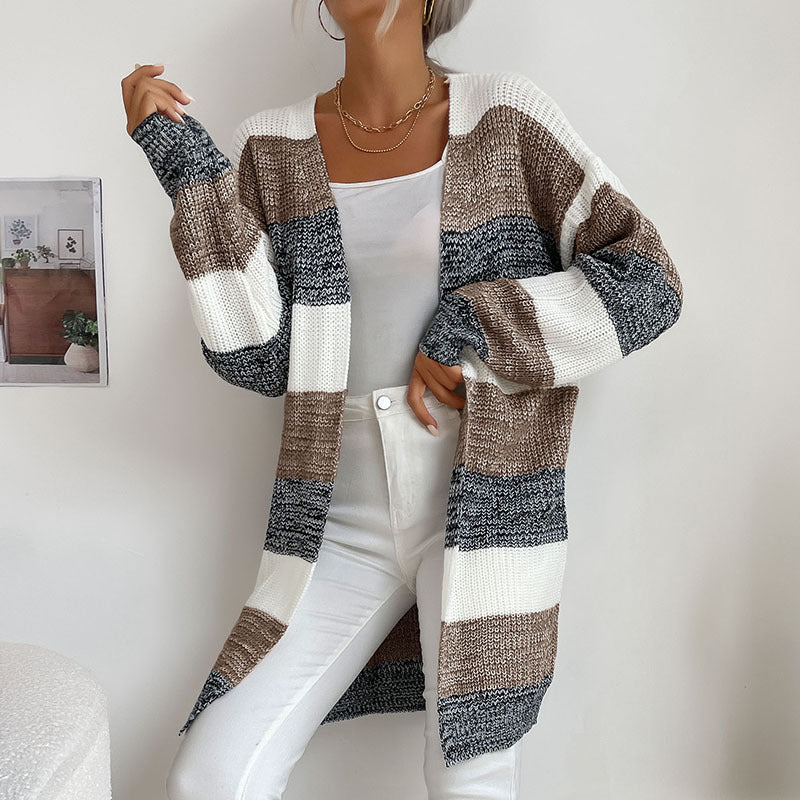 A woman wearing a color block cardigan in white, cream and navy with white cami and white jeans poses against white background with layered gold necklaces