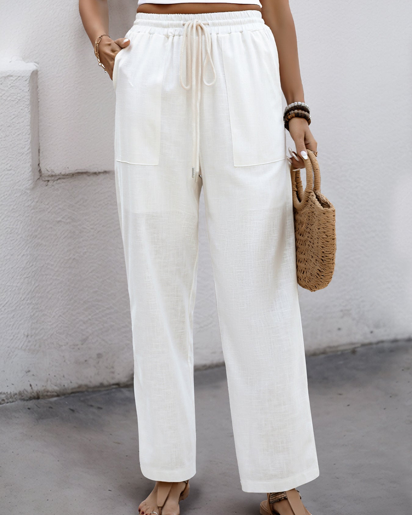 Woman wearing white wide-leg linen pants with an elastic drawstring waist, styled with a crop top and sandals.