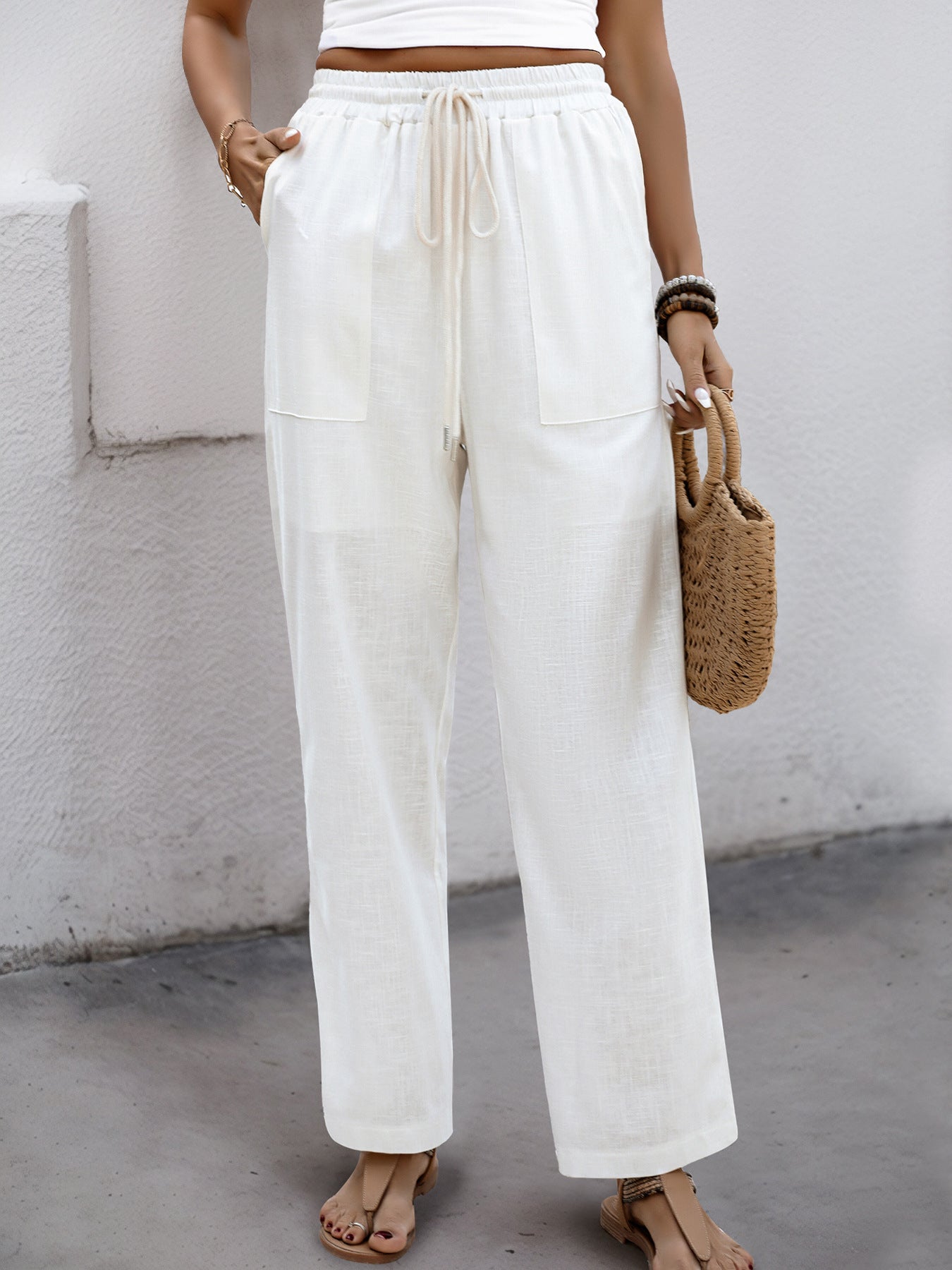 Woman wearing white wide-leg linen pants with an elastic drawstring waist, styled with a crop top and sandals.