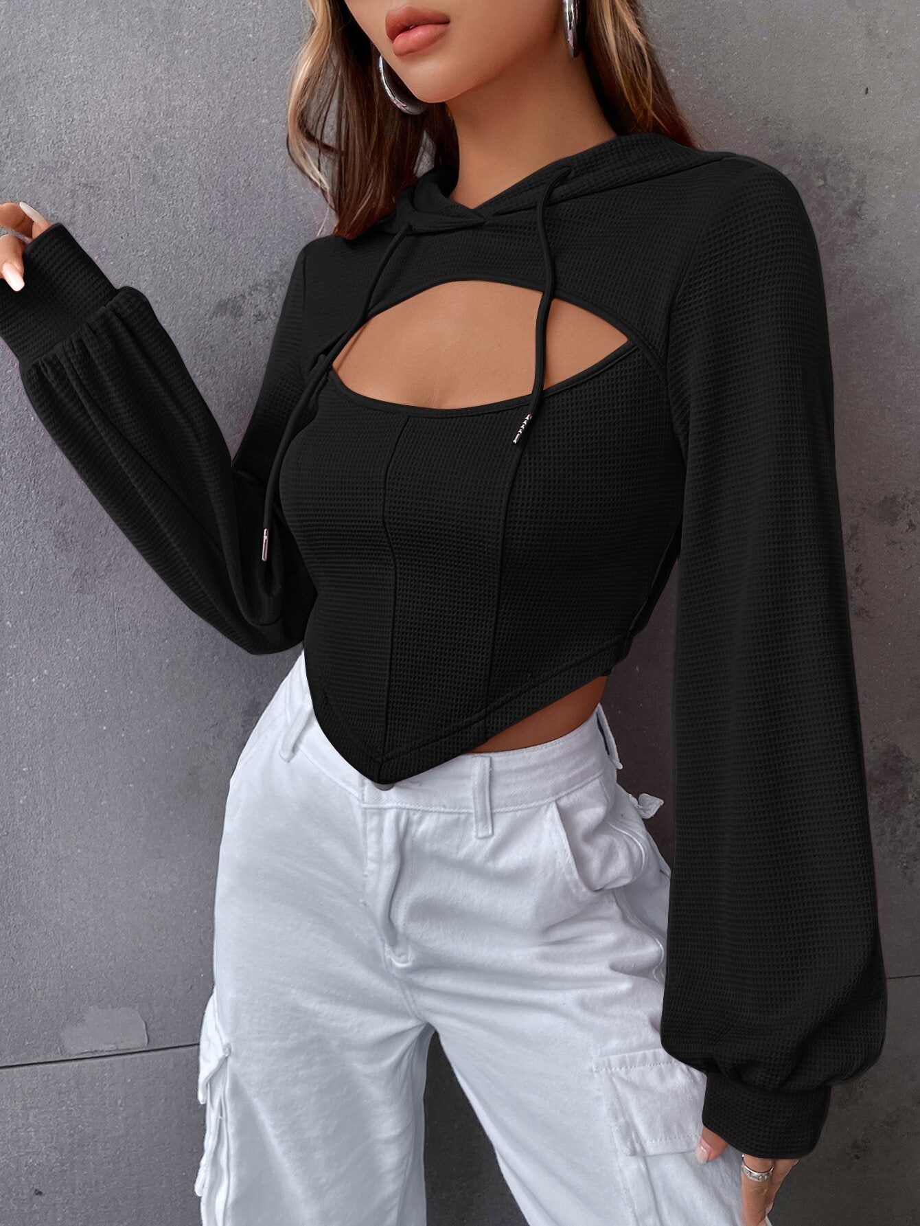 Side profile of woman in black cutout crop hoodie with bishop sleeves and white cargo pants, showing silver hoop earrings