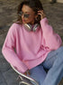 Pink chunky knit sweater worn casually with silver headphones, aviator sunglasses, and light denim jeans, photographed in outdoor setting