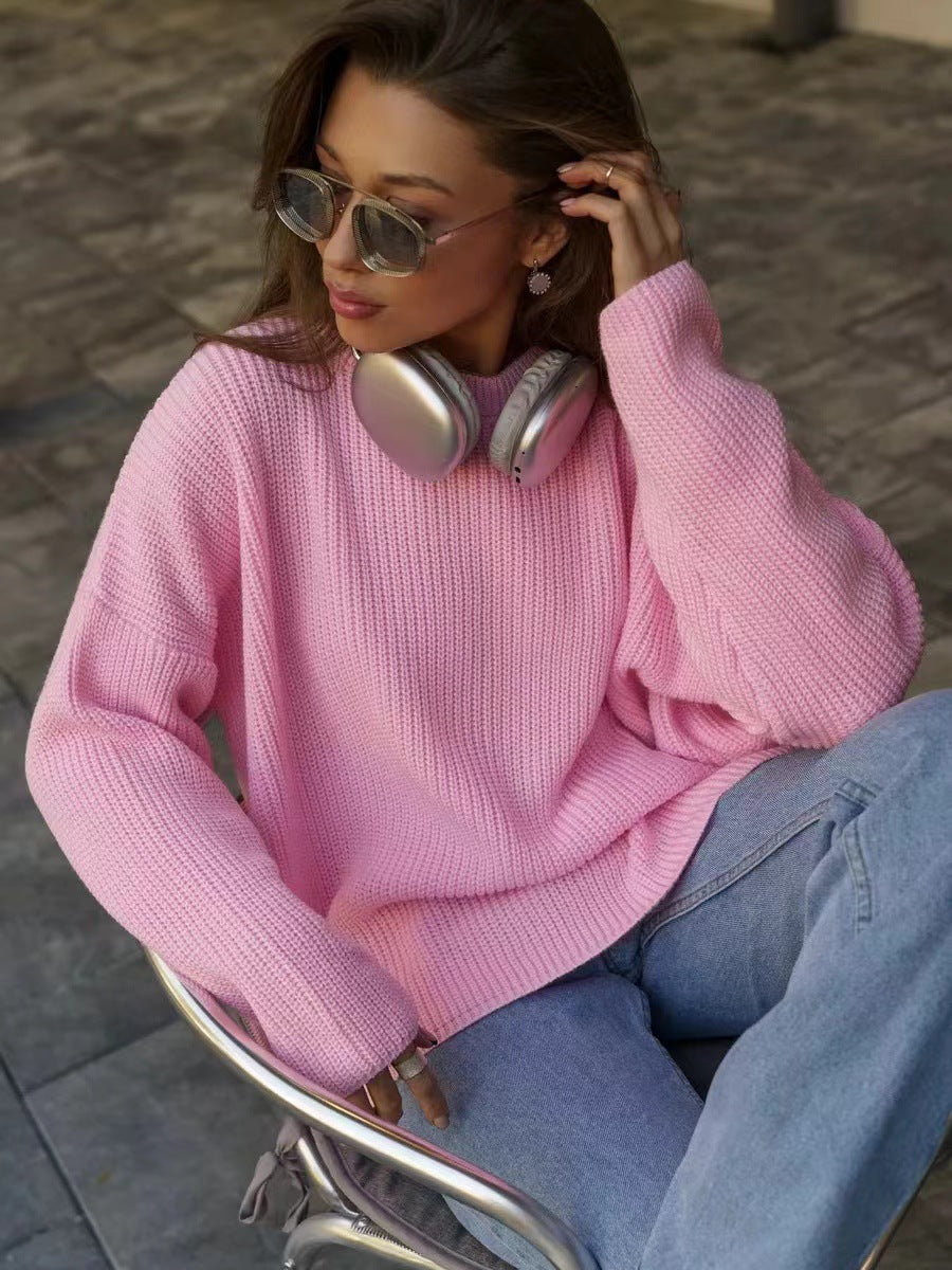 Pink chunky knit sweater worn casually with silver headphones, aviator sunglasses, and light denim jeans, photographed in outdoor setting