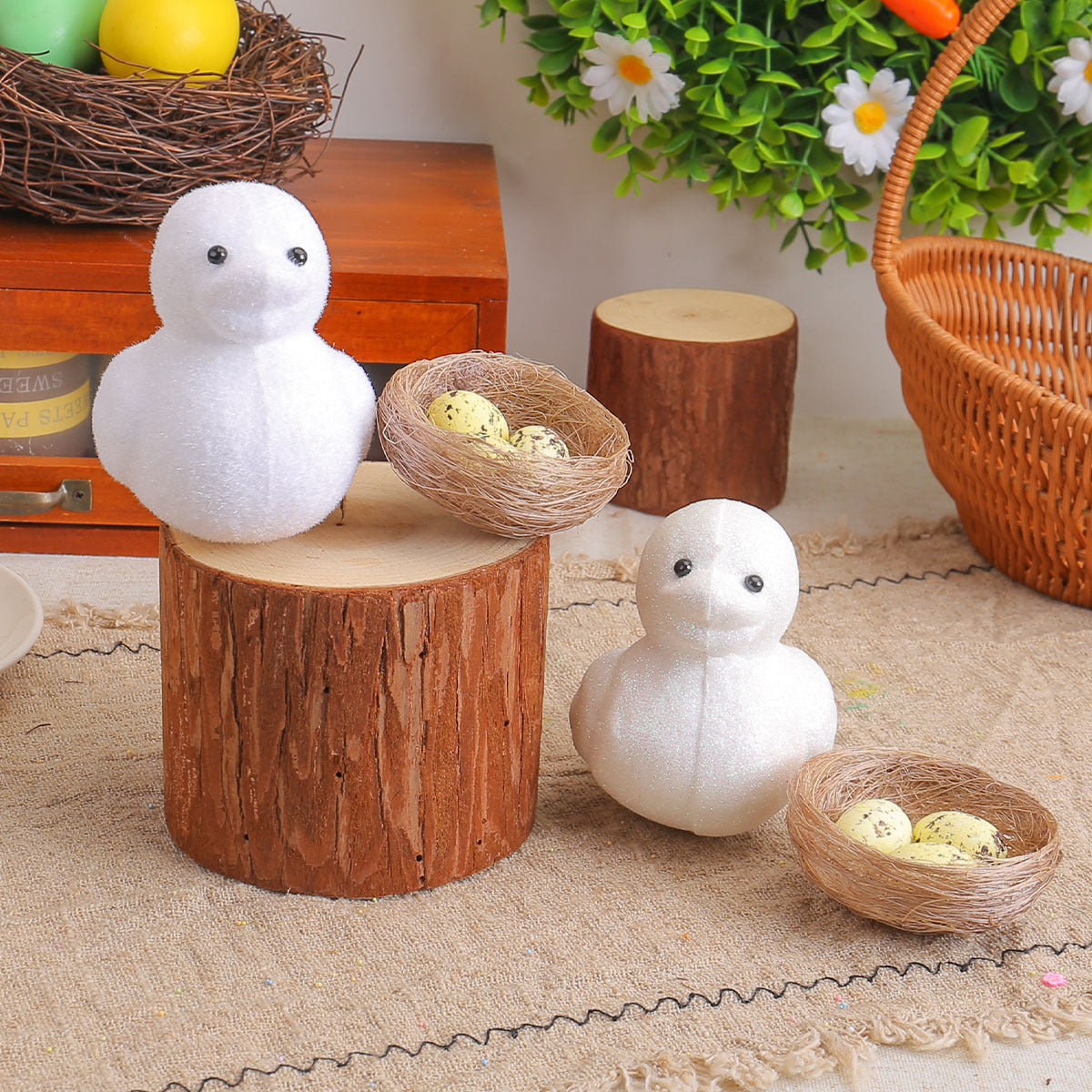 Two white chick figurines with glittery surfaces, set on rustic wooden logs, with decorative nests containing speckled eggs.