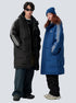 A man and woman are posing side by side against a gray background. Both wearing Benedictory puffer parkas with triple stripe sleeves and oversized fit