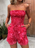 Front view of a woman in a red strapless smocked romper with a drawstring waist and pockets.