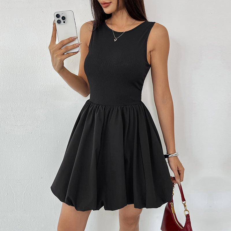 A woman wearing a black sleeveless dress, holding a smartphone while carrying a red handbag, accessorized with a delicate necklace and silver bracelet.