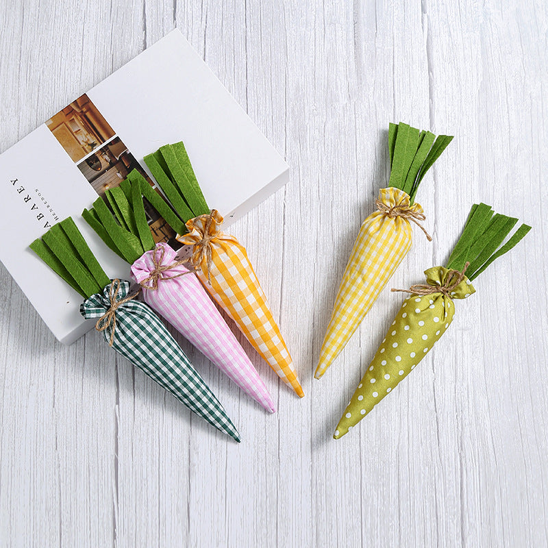 Five decorative fabric carrots in different patterns and colors, resting on a white book against a white wooden surface.