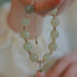 Hand holding a jade bead bracelet with a gold adjustable chain and a dangling pink cherry charm