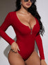 Close-up of a woman in a red ribbed bodysuit with a silver zipper, accessorized with silver earrings and sunglasses, highlighting her neckline.
