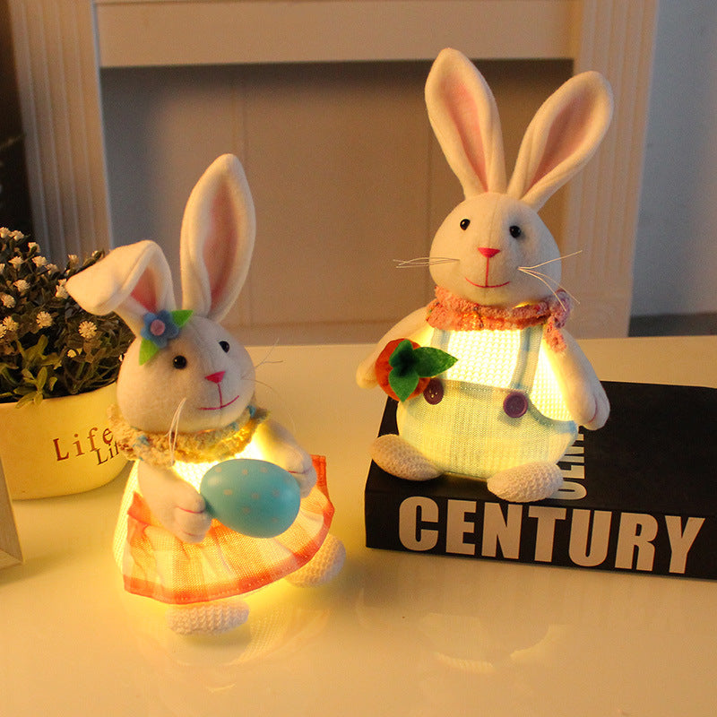 A pair of illuminated plush bunny decorations on a tabletop, one holding a carrot, the other holding an Easter egg, with soft lighting in the background.