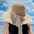 A woman in a straw sun hat with a wavy brim and lace ribbon, gazing at a bright sky and open waters.