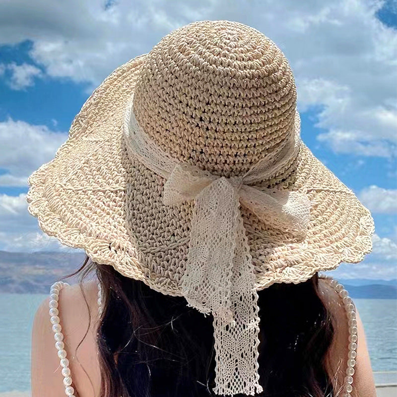 A woman in a straw sun hat with a wavy brim and lace ribbon, gazing at a bright sky and open waters.