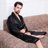 Man seated on a beige tweed sofa wearing an untied black silk robe, looking directly at camera in a minimalist white interior setting