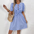  A model poses outdoors wearing a blue striped dress with a fitted waist, puff sleeves, and bow-tie front details, holding a woven bag.