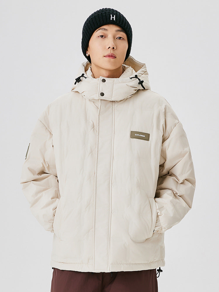 A man wearing a black ribbed beanie and cream puffer jacket with EXPLORERA logo, standing against white background