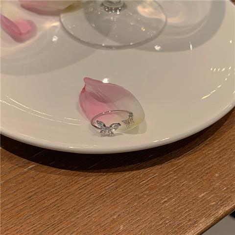 Silver butterfly ring displayed on a white plate with pink flower petals