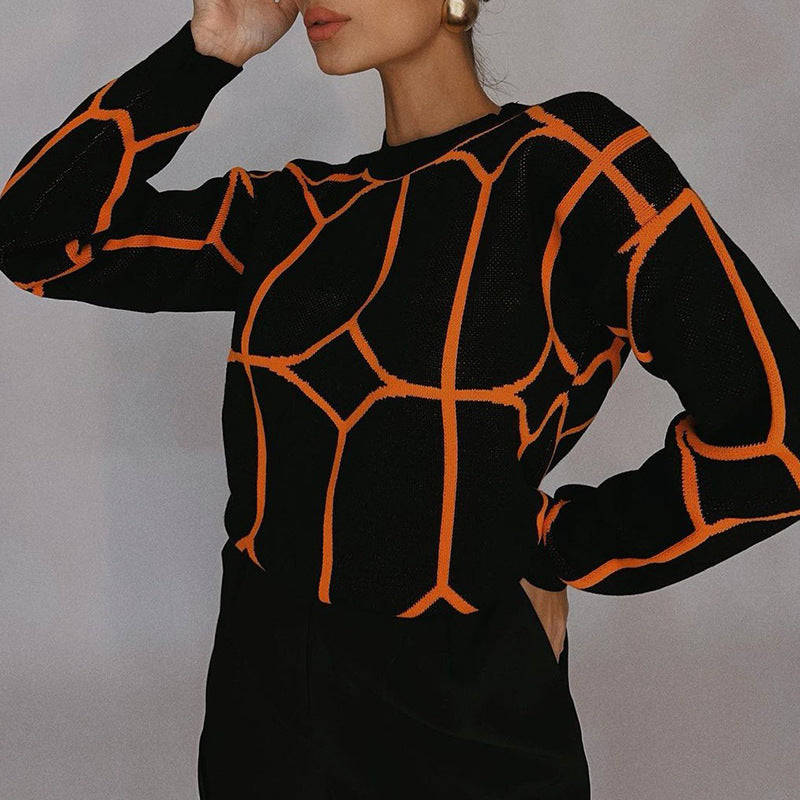 A model is posing with hand raised wearing a black sweater with orange geometric pattern against neutral gray background