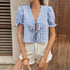 Woman in a blue gingham puff sleeve crop top with a deep V-neck and front tie closures, styled with white distressed shorts and gold jewelry.