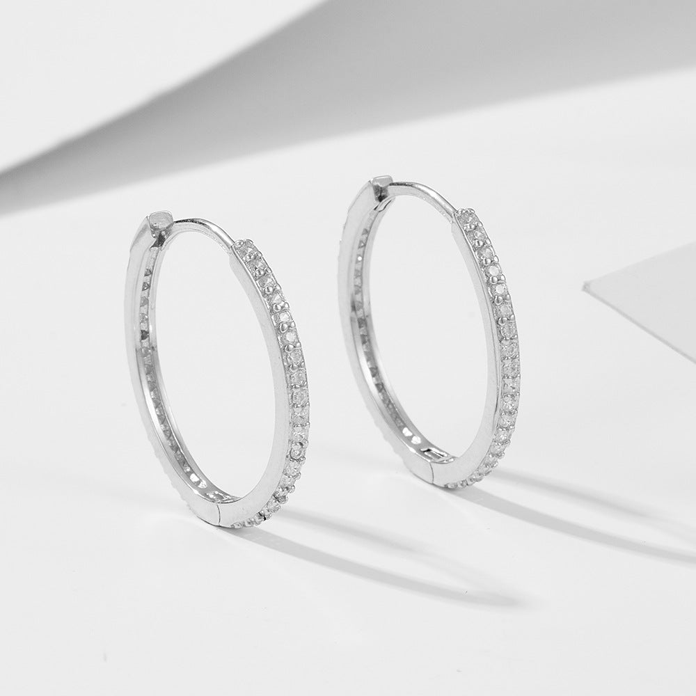 Silver pave diamond hoop earrings displayed on white geometric surface. The sleek sterling hoops showcase brilliant crystals along the outer rim
