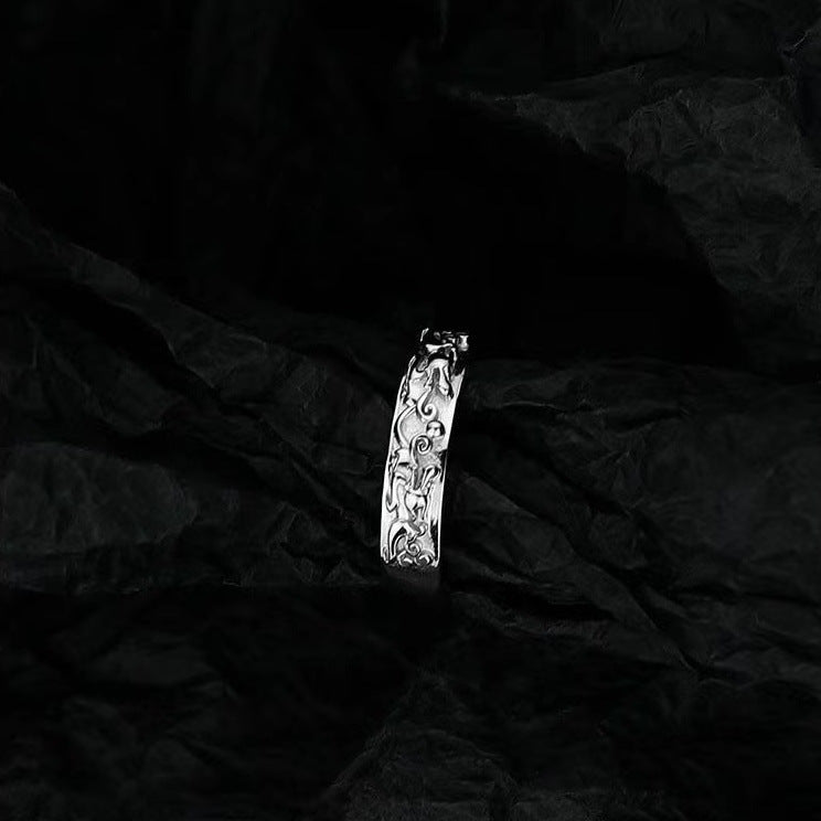 Artistic shot of silver engraved band ring against textured black background highlighting relief pattern