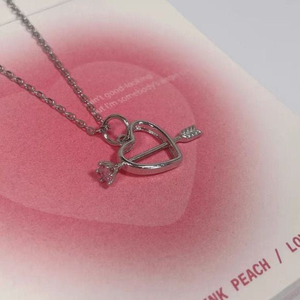 Silver heart pendant with arrow detail on pink gradient heart background, close-up view