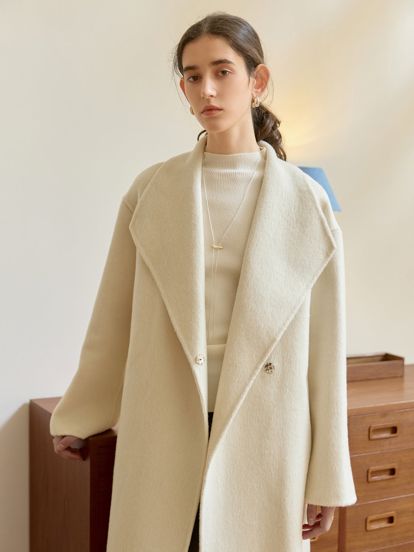 Close-up of cream wool coat's wide lapel and gold bar necklace styling