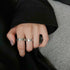 Close-up of hand with mauve nails wearing two matching silver Roman numeral rings with weekday engravings on grey surface