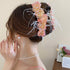 A statement floral hair clip with pink fabric flowers, rhinestones, and delicate white feathers, styled in a romantic updo.