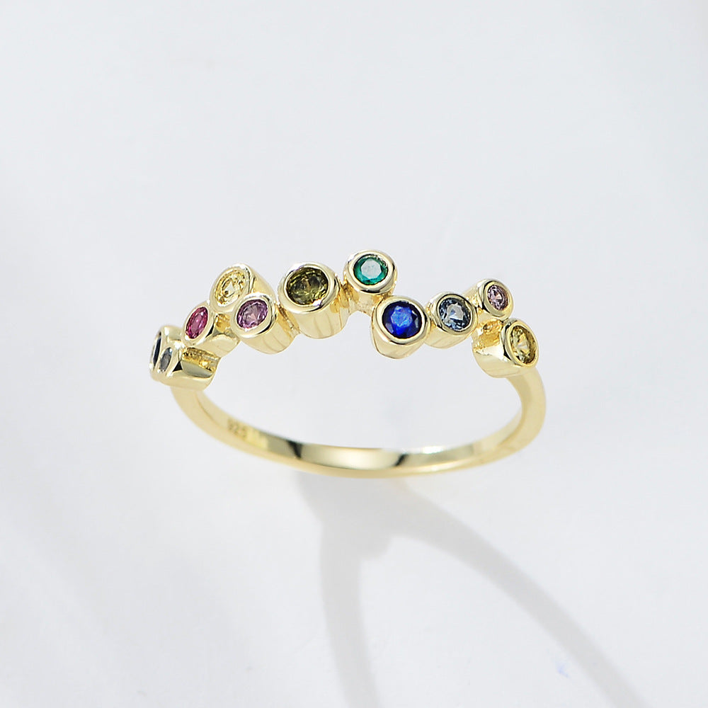 A gold bubble ring with multicolored gemstones arranged in scattered pattern photographed against clean white background