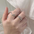 A hand holding white fabric while wearing silver twig-design rings with rose detail, displayed against white satin background