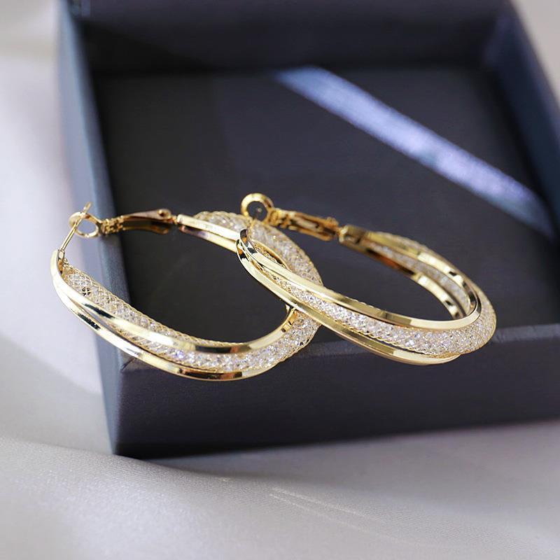Crystal-lined gold hoops displayed on dark presentation box, showing clasp detail