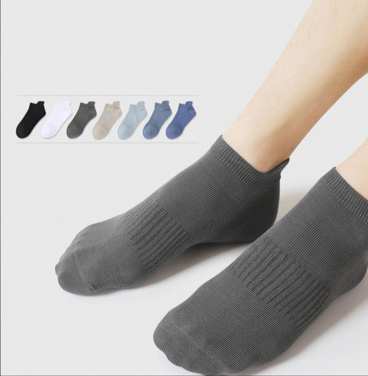 A model is wearing gray ankle socks against white backdrop. Inset shows color range of seven ankle sock options from black to navy in neutral tones
