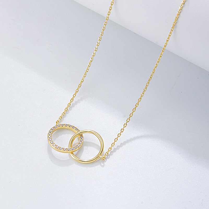 Gold interlocking circles necklace with diamond-encrusted circle and plain circle pendant on delicate chain against angled white surface