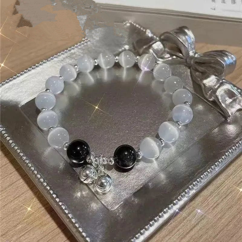A gemstone bracelet with translucent white beads and black accent stones resting on a silver display tray. Includes small silver charm pendants