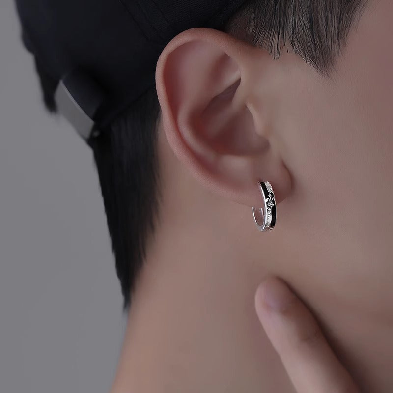 Stainless steel hoop earring with black enamel and fleur-de-lis design worn on ear