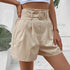 Side view of beige high-waisted shorts showing pleated detail and circular buckle closure