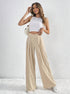 Woman smiling in beige wide-leg trousers with pleats and V-cut high waist.